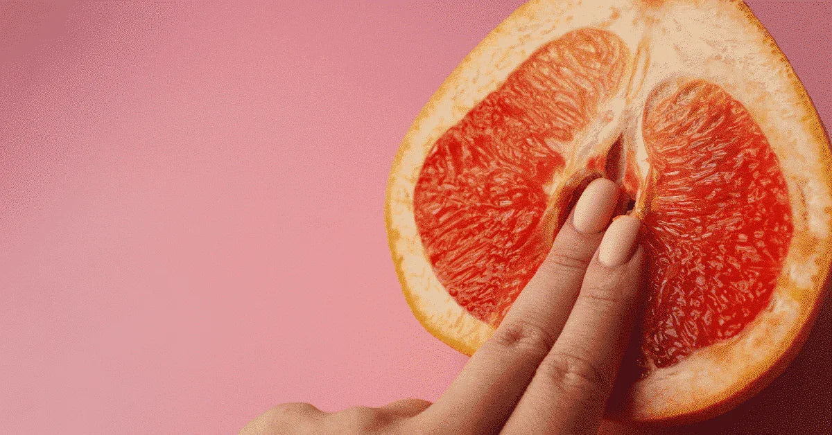 Hand with manicured nails touching sliced grapefruit, symbolizing female sensuality on pink background