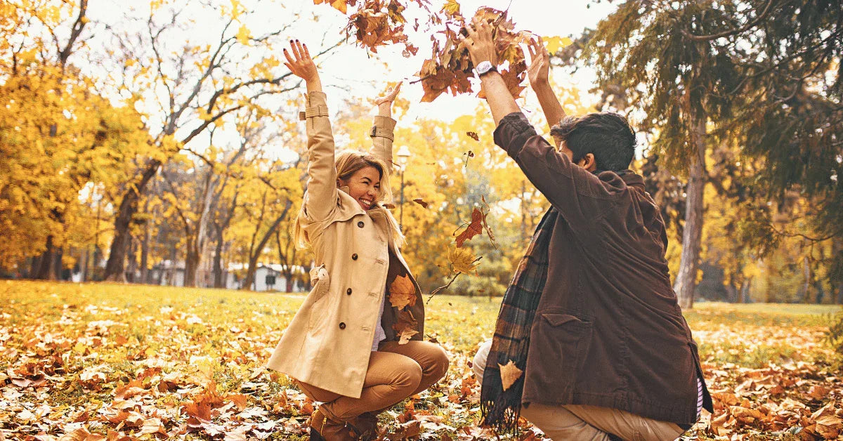 Happy couple playing with autumn leaves in a park, wearing fall coats and scarves