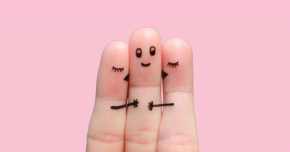 Three fingers with drawn faces and arms hugging, representing intimacy and relationships on pink background.
