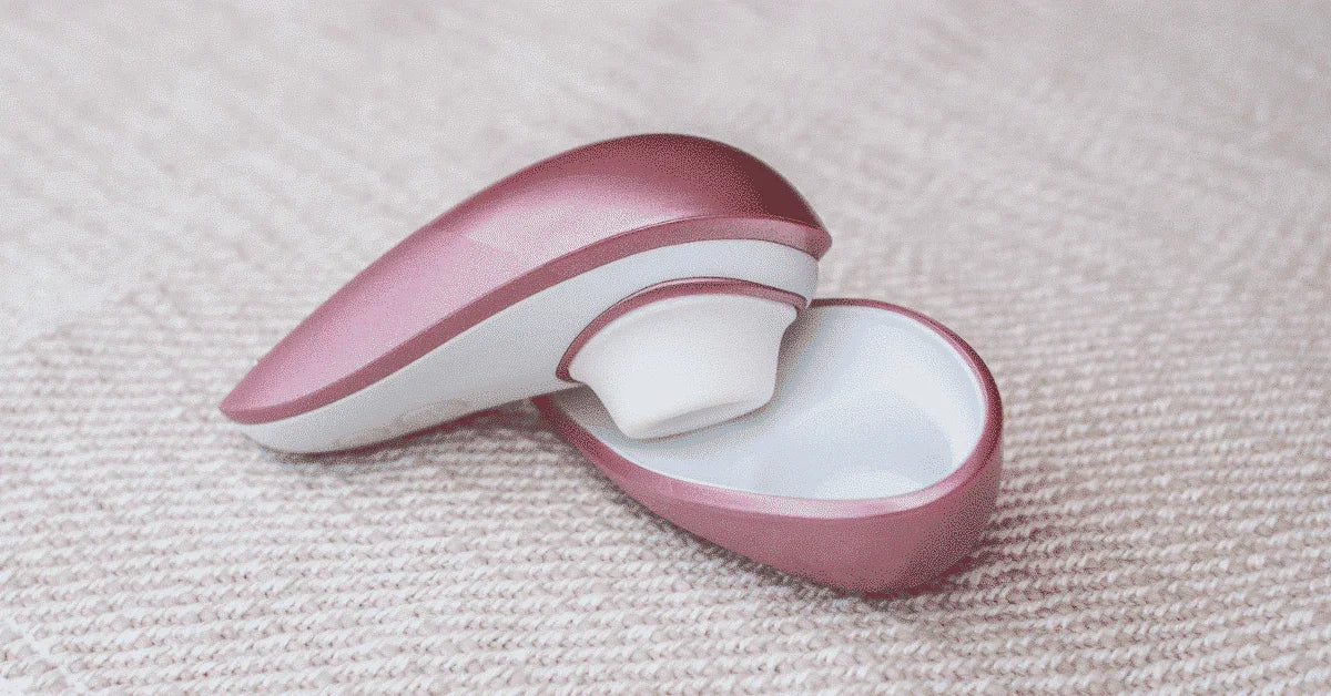 Pink and white Womanizer clitoral stimulator and case on textured fabric surface