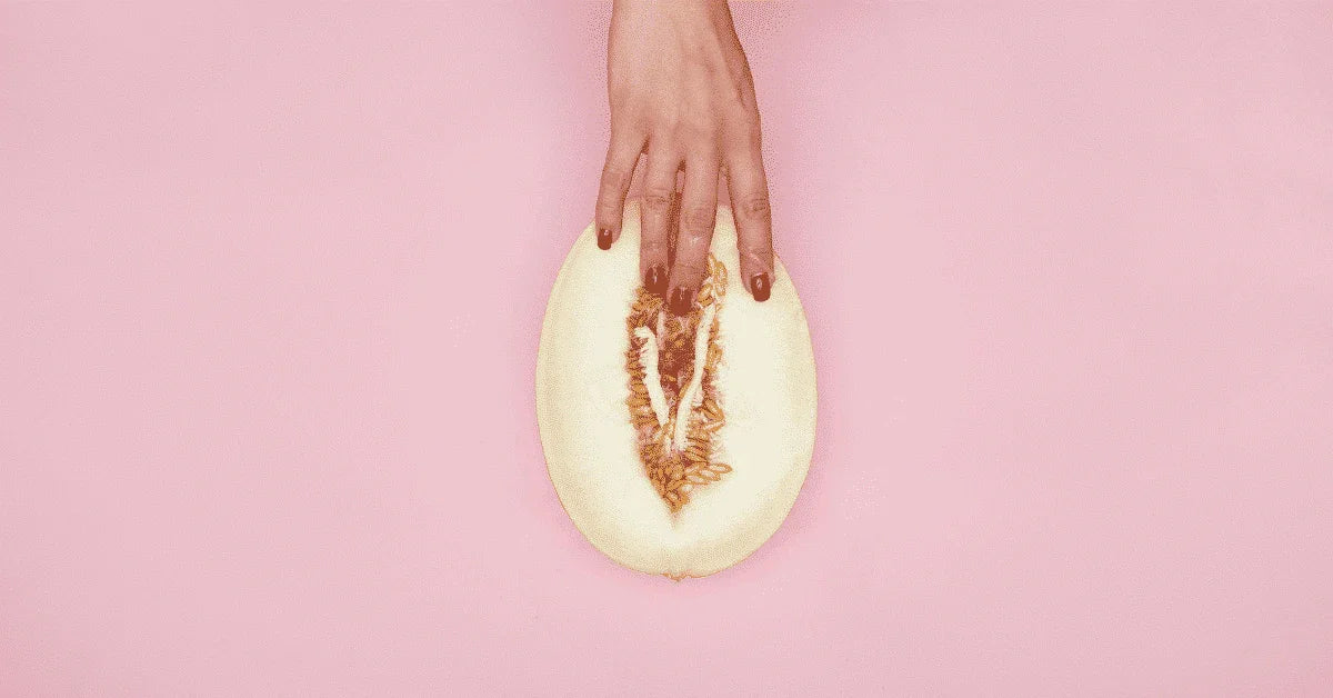 Hand with red nails touching inside of a halved melon on pink background, sensual concept