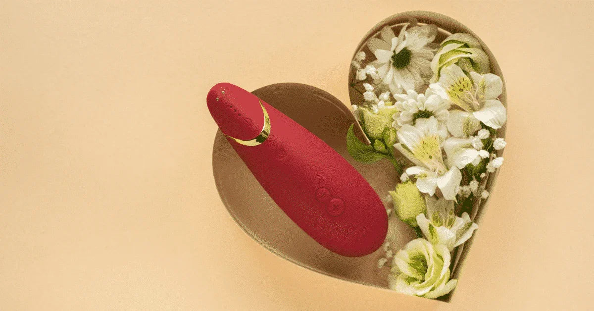 Red personal massager in a heart-shaped box with white flowers on a beige background