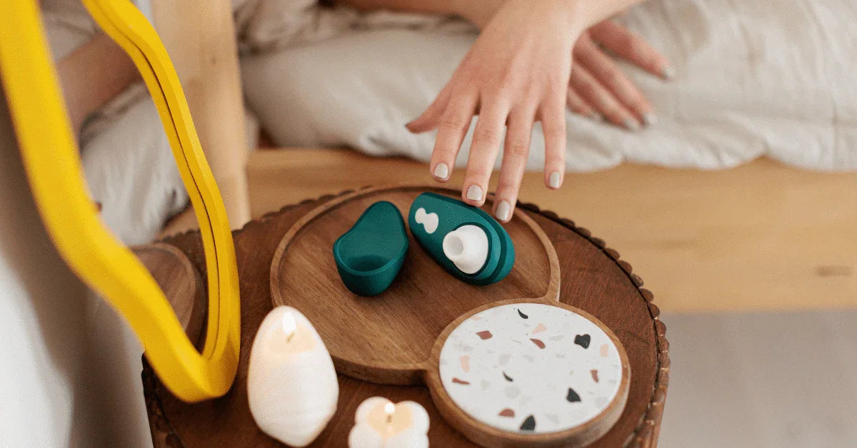 Woman picking up a green personal massager from a bedside table with candles.