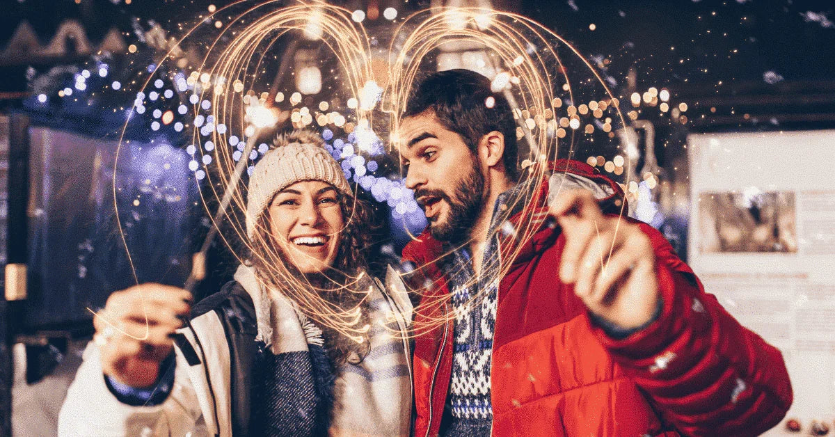 Smiling couple with sparklers forming a heart shape, festive winter background, romance