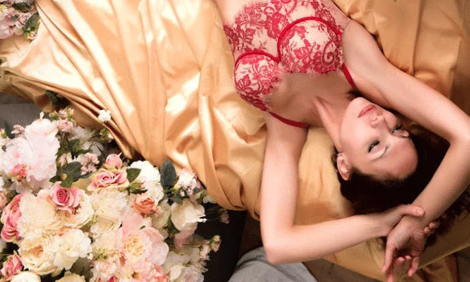 Woman in red lace lingerie lying on gold satin sheets, surrounded by pastel flowers
