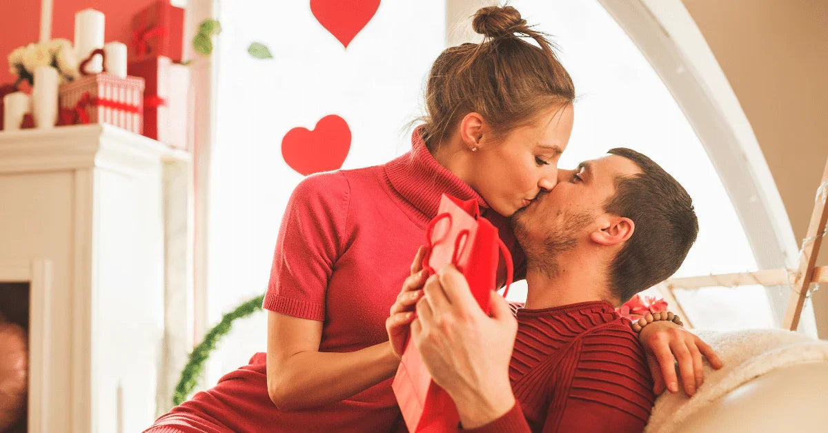Romantic couple kissing on Valentine's Day, exchanging gifts in a cozy, decorated living room