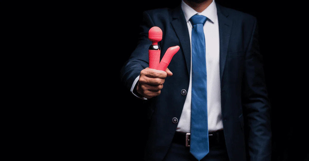 Man in suit holding a pink couples vibrator and massager in front of a dark background