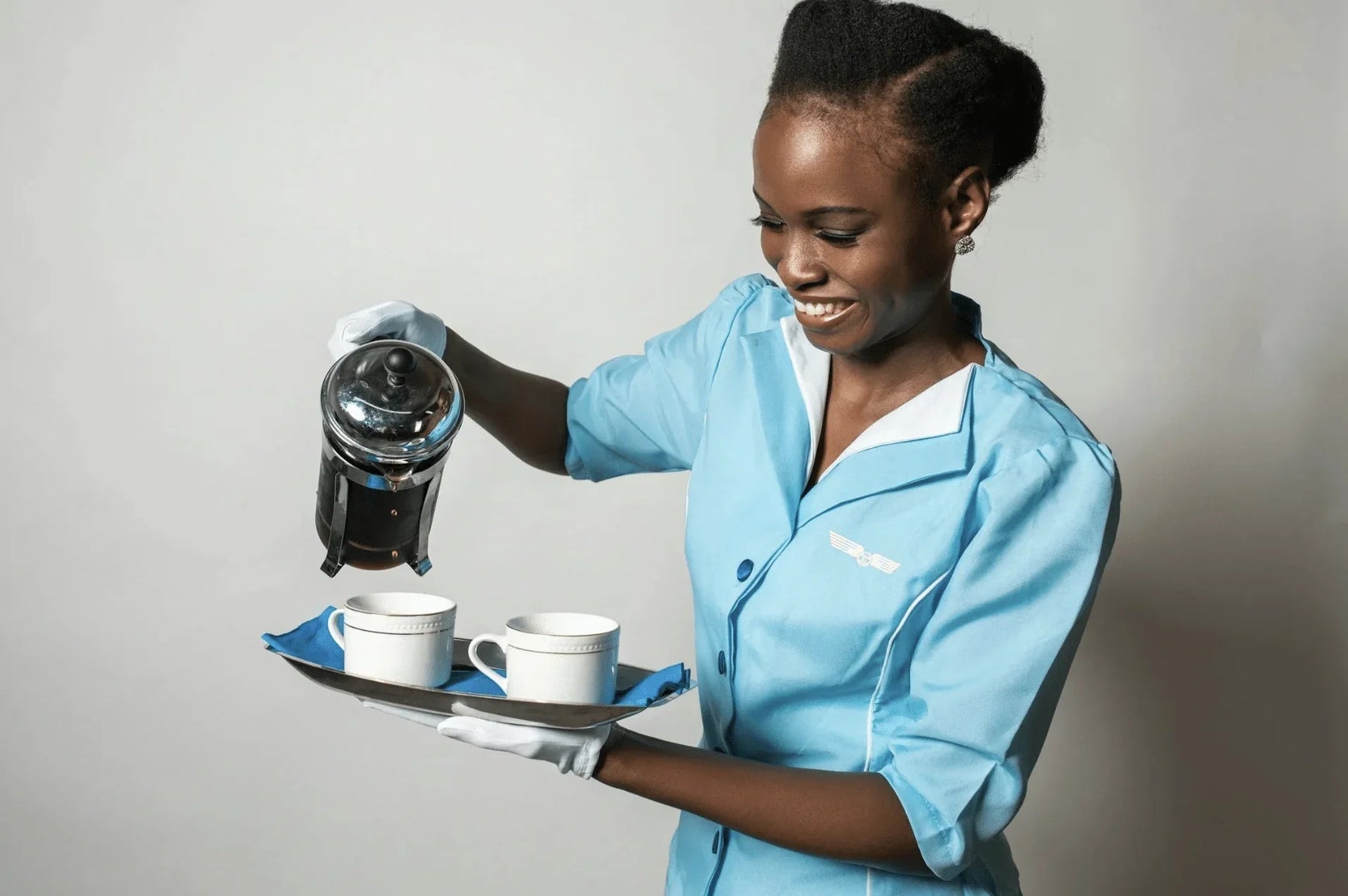 Smilende servitør i blå uniform serverer kaffe med fransk press på sølvfat