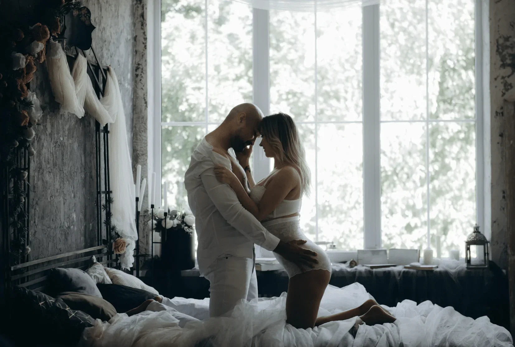 Romantic couple in white lingerie embracing on a bed in a softly lit bedroom