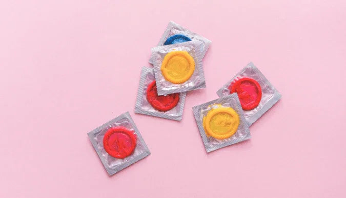 Fargerike kondomer i pakninger på rosa bakgrunn, perfekt for par og voksne
