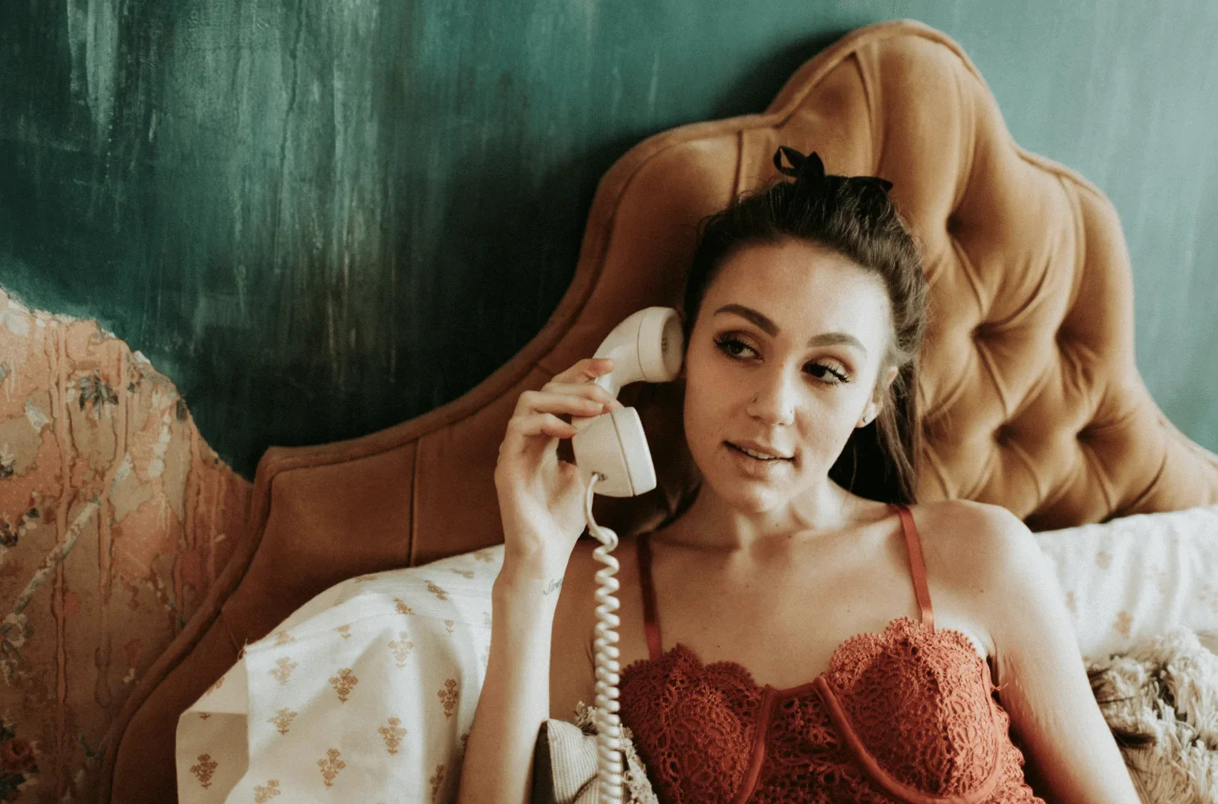 Woman in red lace lingerie sitting on bed, talking on vintage phone, in cozy bedroom