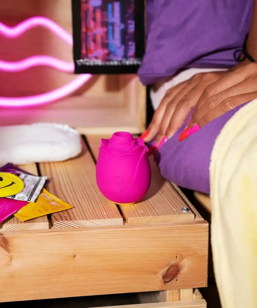 Pink rose-shaped personal massager and colorful condoms on bedside table