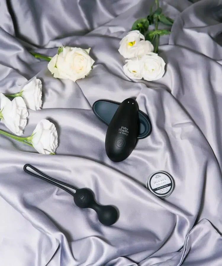 Black intimate products and white roses on silky grey fabric, Fifty Shades collection