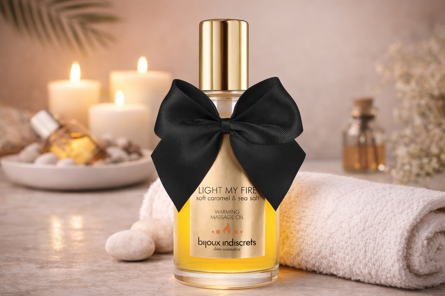 Massage oil with black bow, candles, stones, and towel in a relaxing spa setting