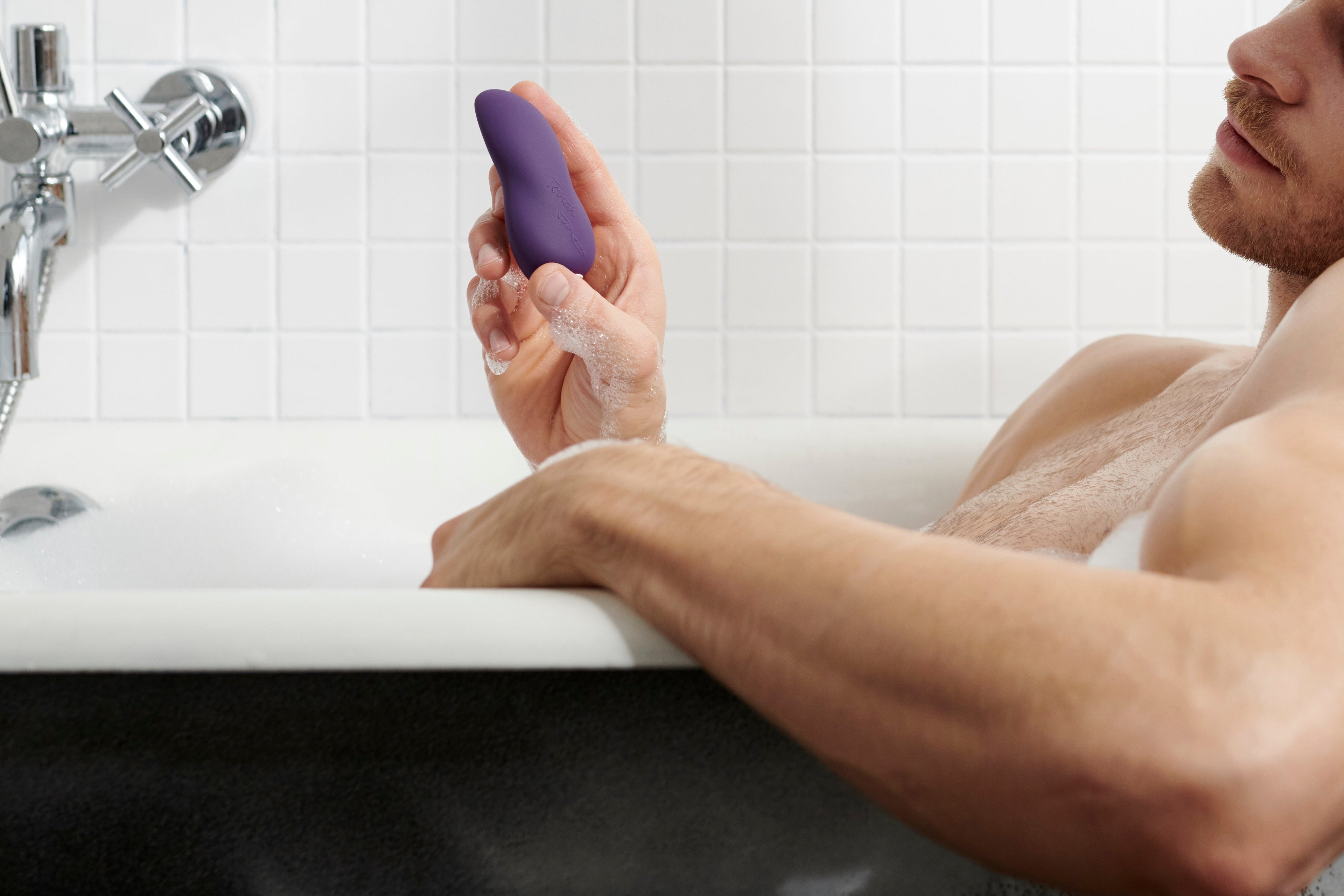 Man in bathtub holding waterproof purple vibrator for adult pleasure