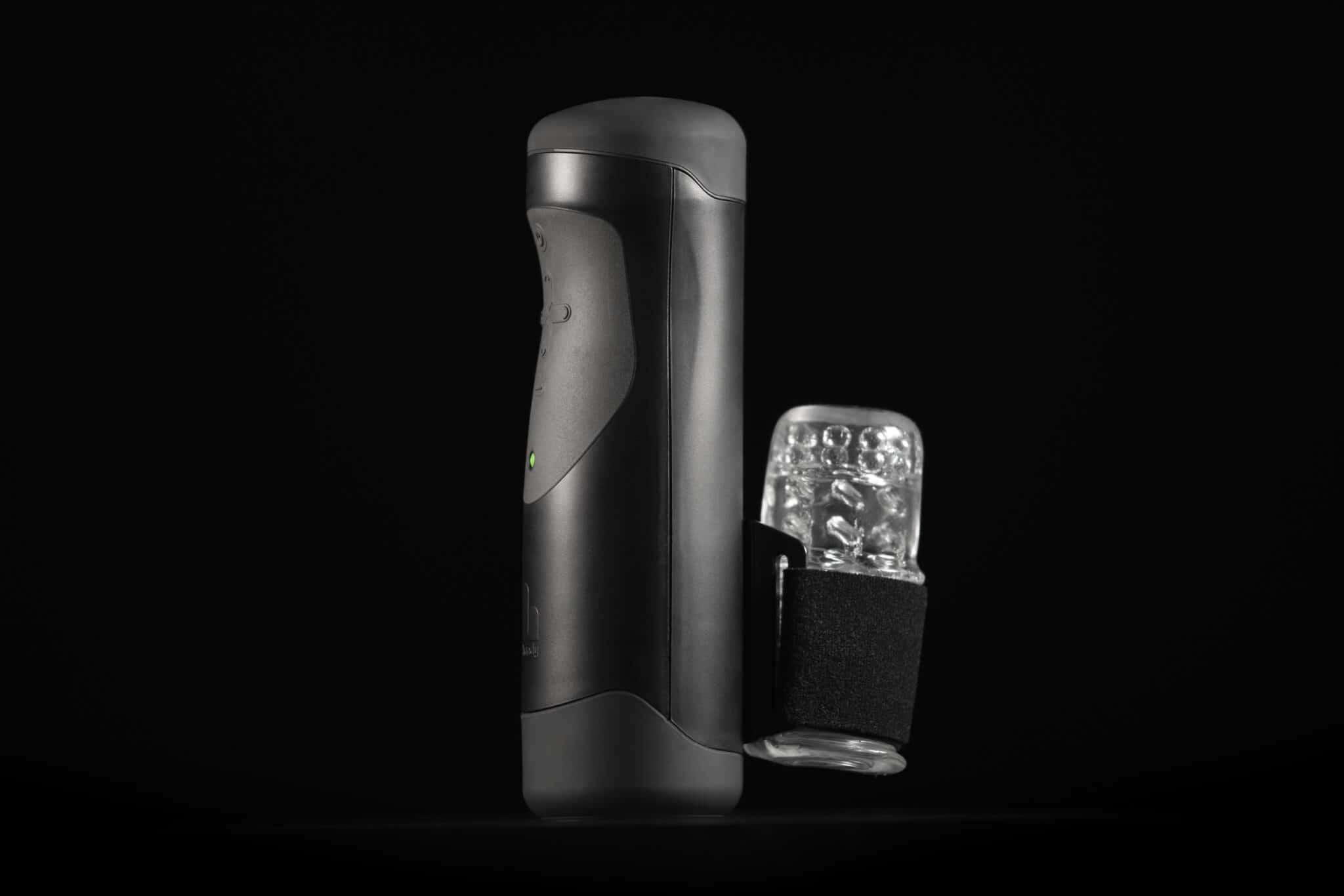 Black and clear male pleasure device with textured sleeve on dark background.