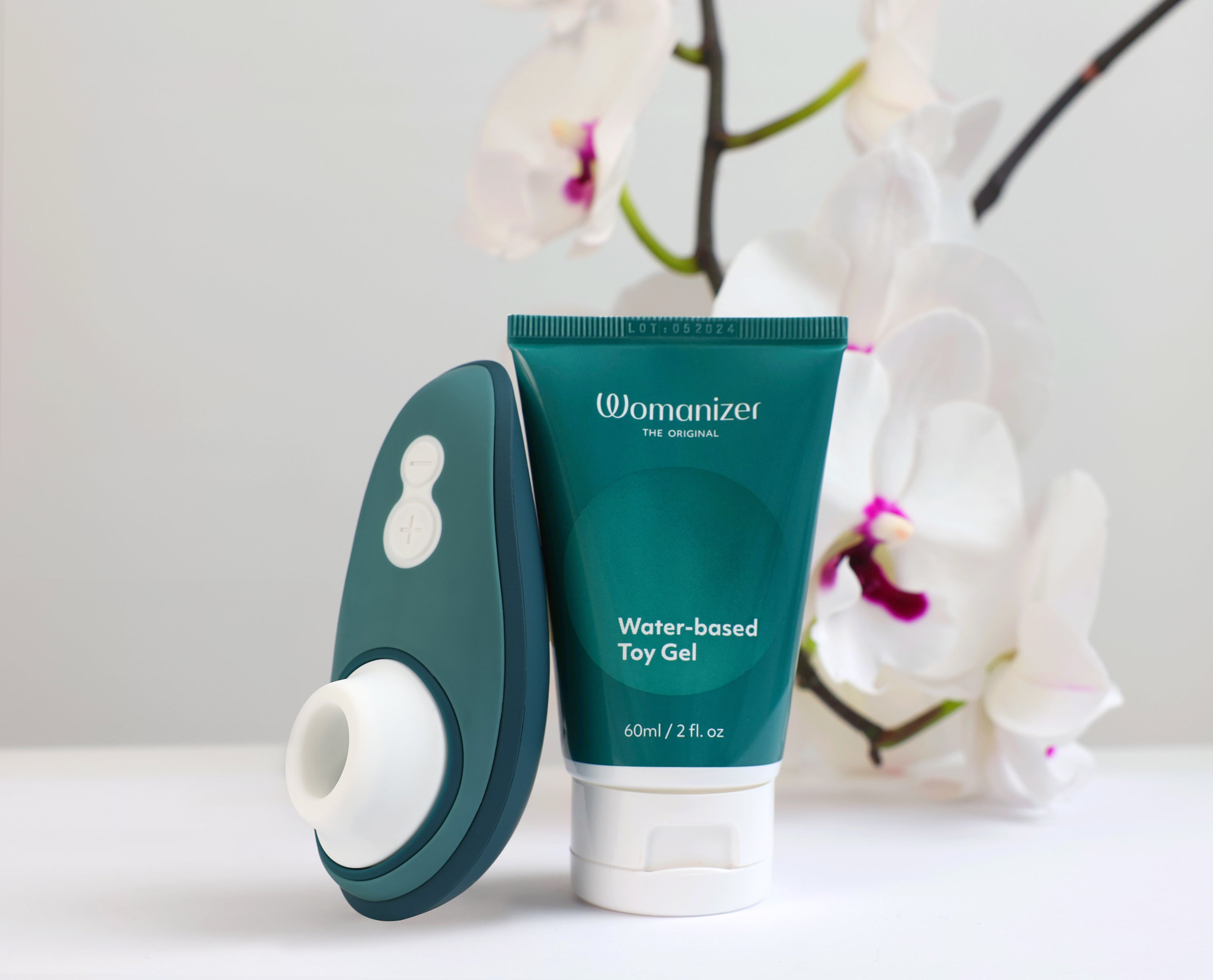 Water-based toy gel and teal pleasure device displayed with white orchid background