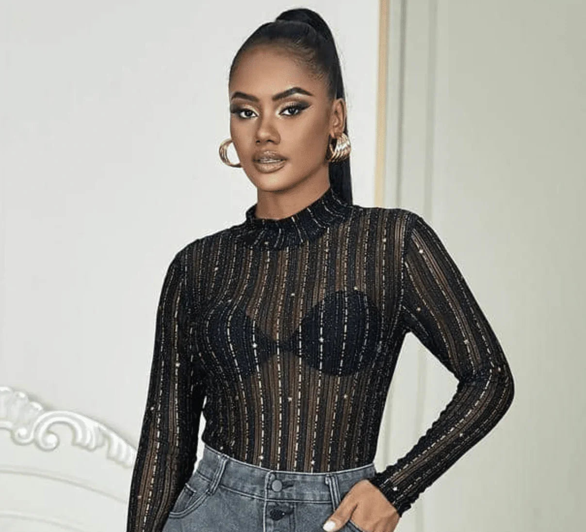 Woman wearing sheer black lace long-sleeve top with striped pattern and high-waisted jeans