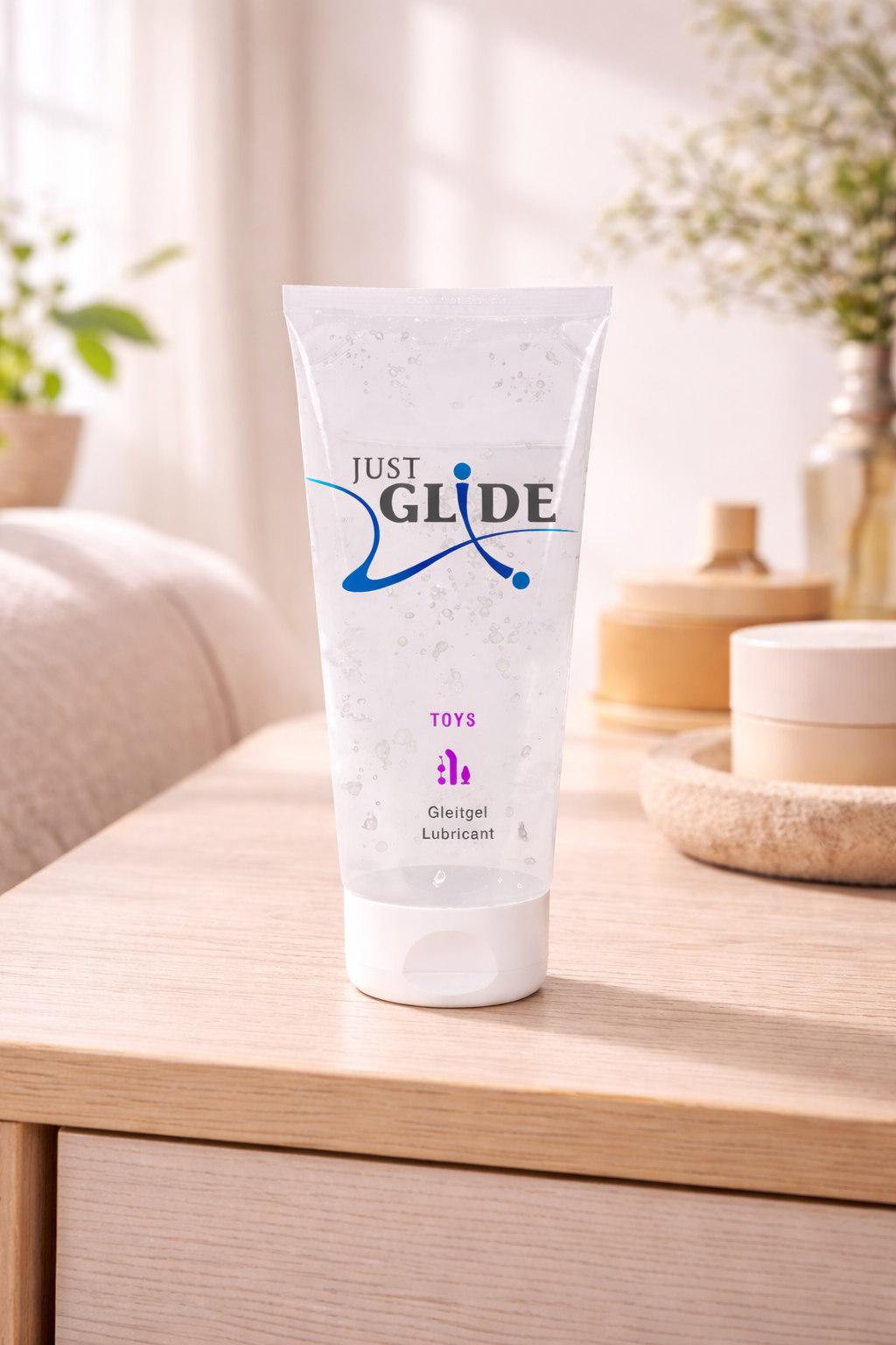 Clear tube of Just Glide lubricant gel for toys on a wooden surface in a softly lit room