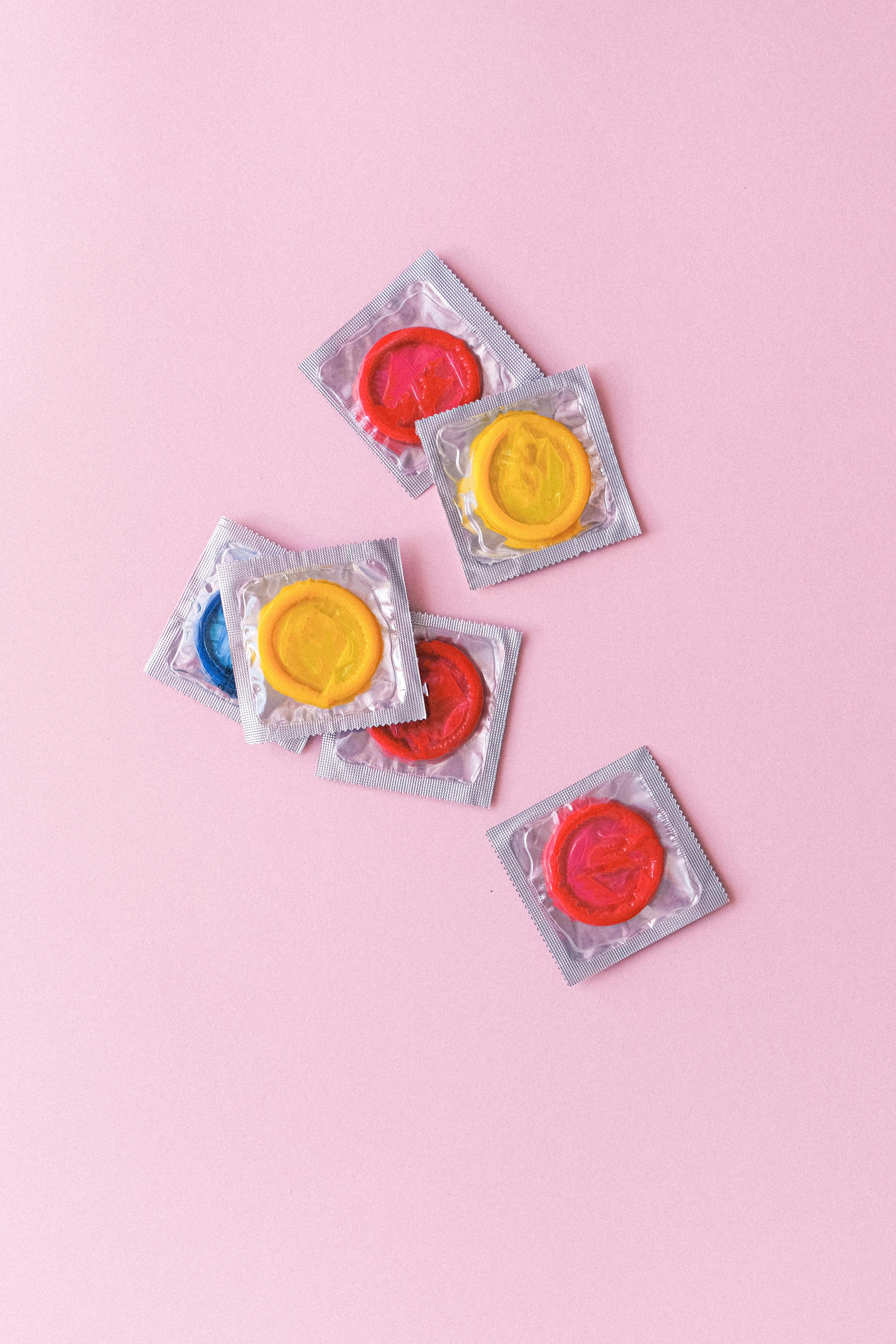 Assorted colorful condoms in wrappers on a pink background, safe sex products