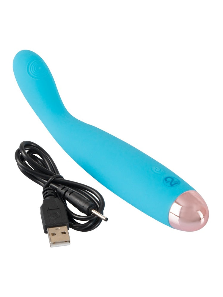 Turkis mini-vibrator liggende diagonalt med USB-ladekabel ved siden av