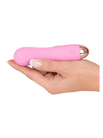 Hånd holder Cuties rosa rillet minivibrator liggende i håndflaten med roségullfarget bunn synlig, viser den kompakte størrelsen.