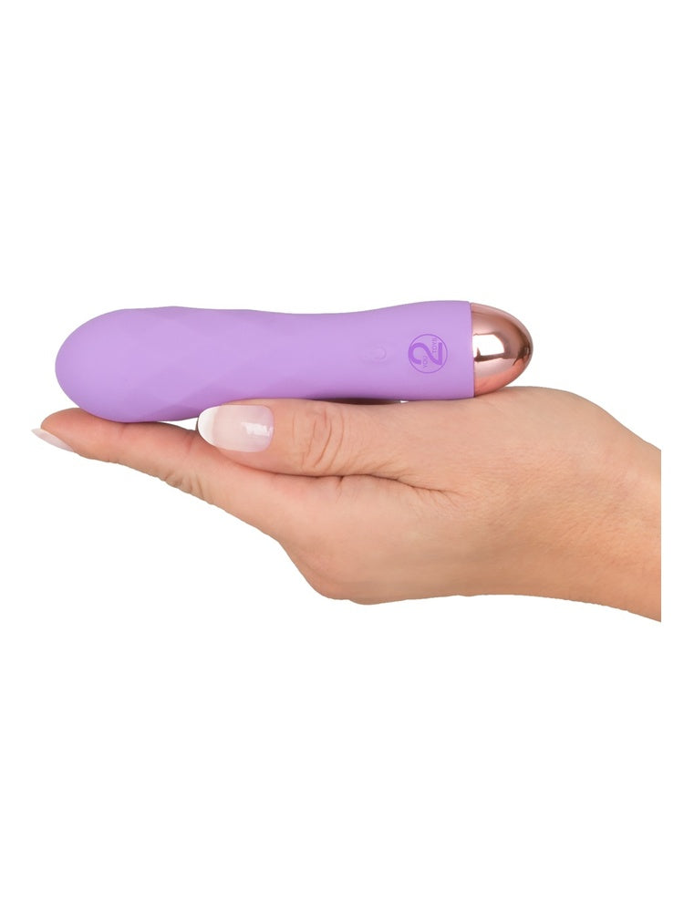 Hånd holder Cuties lilla minivibrator liggende i håndflaten, viser den kompakte størrelsen og roségullfarget bunn.