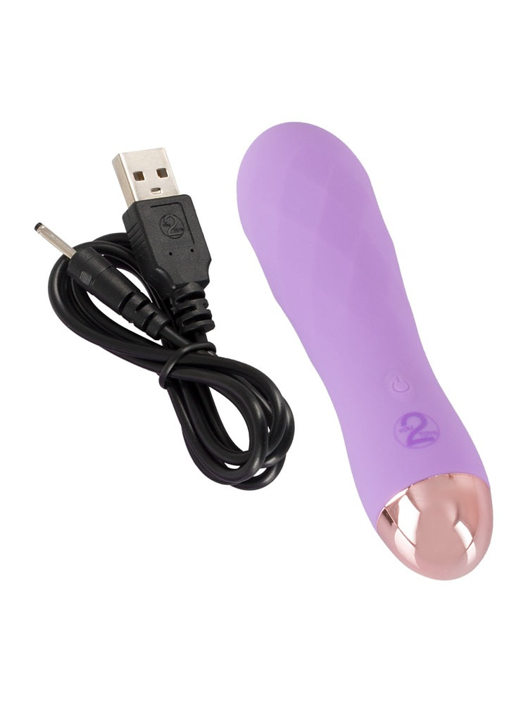 Cuties lilla minivibrator med medfølgende svart USB-ladekabel plassert ved siden av mot hvit bakgrunn.