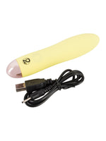Cuties gul minivibrator med tillhörande svart USB-laddningskabel liggandes bredvid varandra mot vit bakgrund.