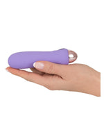 Hånd holder Cuties minivibrator i lilla liggende i håndflaten, viser den kompakte størrelsen.