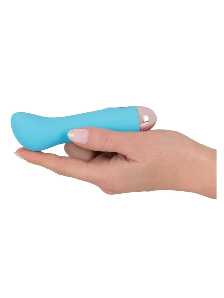 Hånd holder Cuties blå minivibrator liggende i håndflaten med buet tupp oppover, viser den kompakte størrelsen.