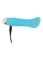 Cuties blå minivibrator med USB-ladekabel koblet til ladeporten i bunnen, mot hvit bakgrunn.