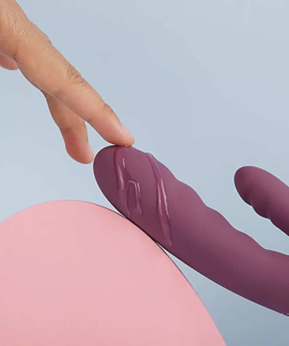 Purple silicone vibrator with lubricant, finger touching tip, intimate product close-up