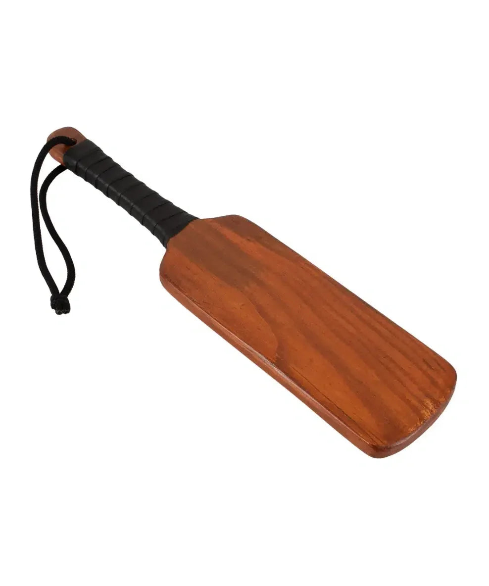 Wooden paddle with black handle and wrist strap, adult novelty accessory on white background