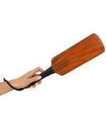 Hand holding a wooden spanking paddle with black handle strap, isolated on white background