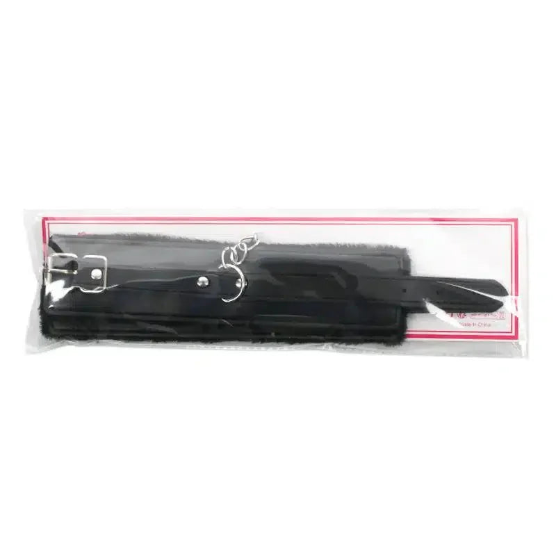 Black faux leather wrist restraints with metal buckle and connector in clear packaging