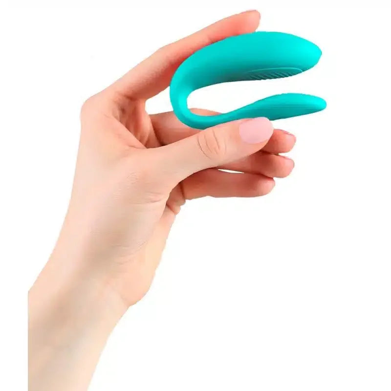 Hand holding a turquoise silicone couples vibrator against a white background