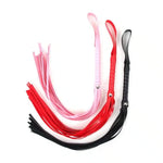 Three faux leather floggers in pink, red, and black with looped handles on white background