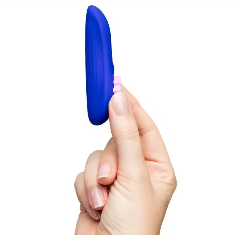Hand holding slim blue silicone vibrator with pink textured control on white background