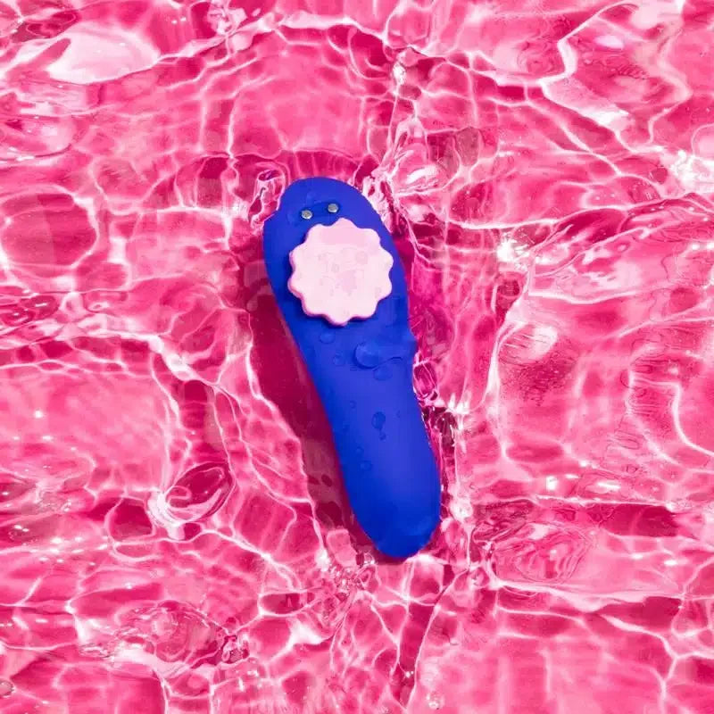 Blue waterproof personal massager with pink detail floating in rippling pink water