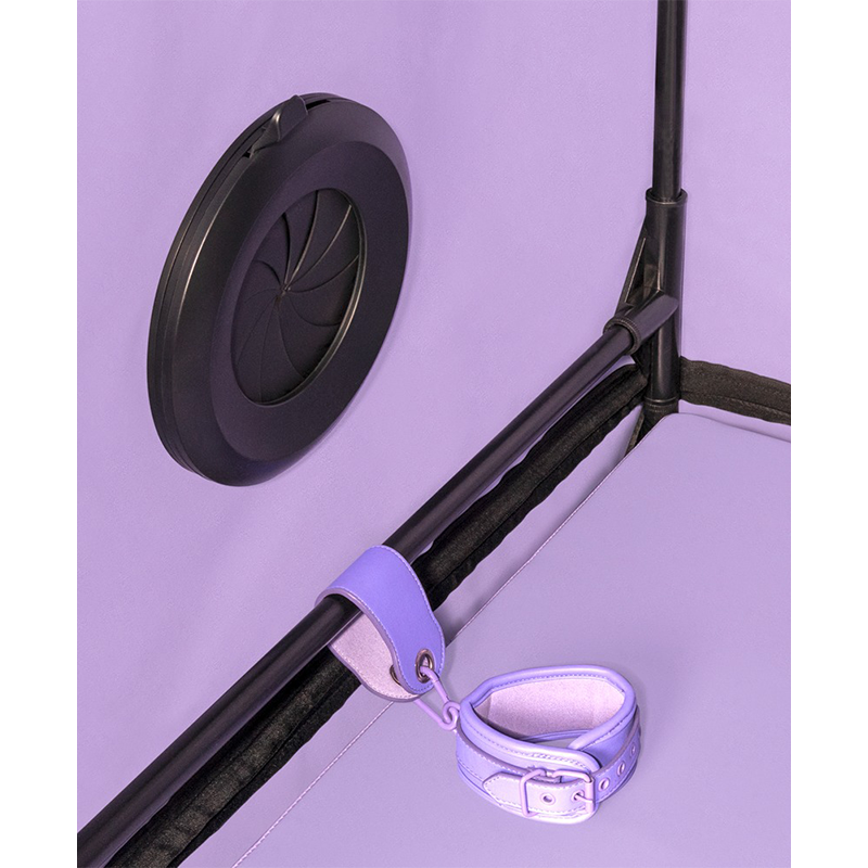 Lilla håndjern og sort ventil festet til ramme, bondageutstyr mot lilla bakgrunn