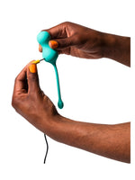 ROMP Cello Vibrerende Egg – hender med oransje negler kobler gul USB-ladekabel til sexleketøyet, hvit bakgrunn.