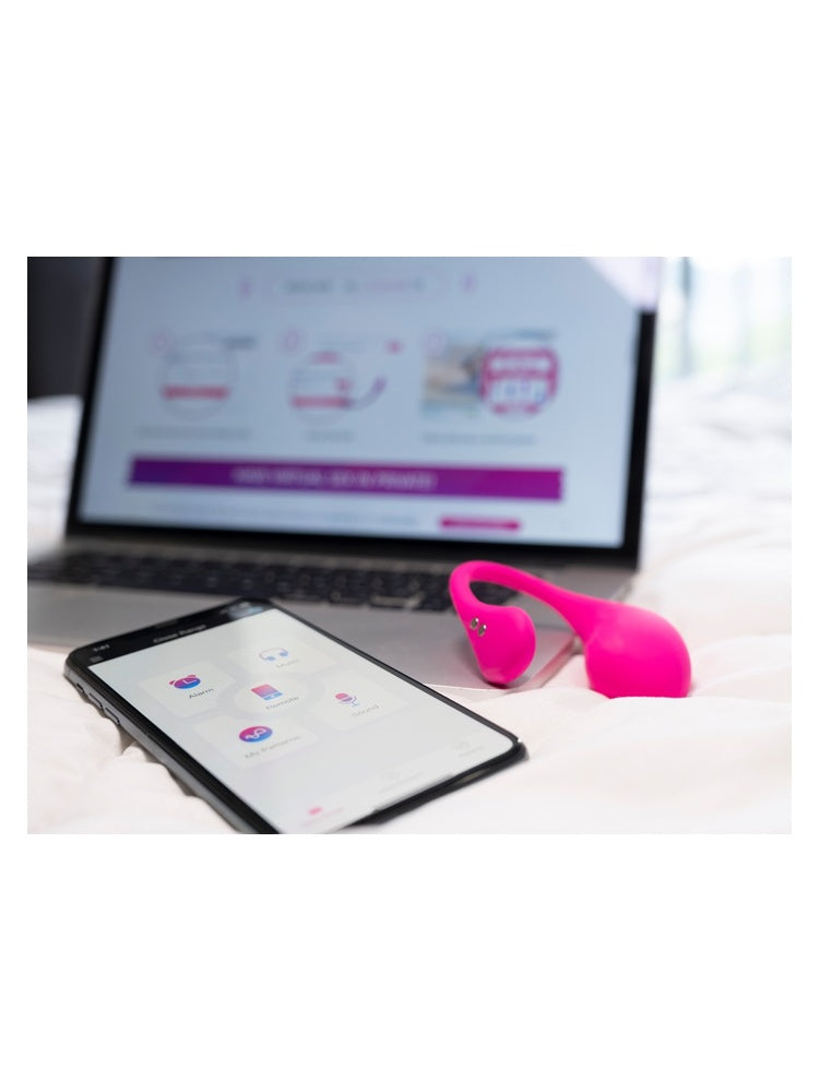Livsstilsbilde: Lovense Lush 3 og smarttelefon med appen plassert på en seng foran en åpen laptop.