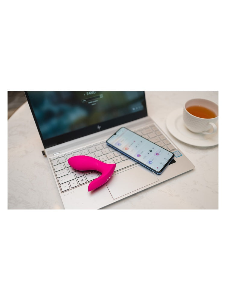 Livsstilsbilde: Lovense Flexer og smarttelefon med appen liggende på tastaturet til en laptop, med en kopp te ved siden av.