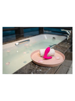 Livsstilsbilde: Lovense Flexer plassert på en rosa tallerken med hvitt håndkle, ved kanten av et badekar med kronblader.
