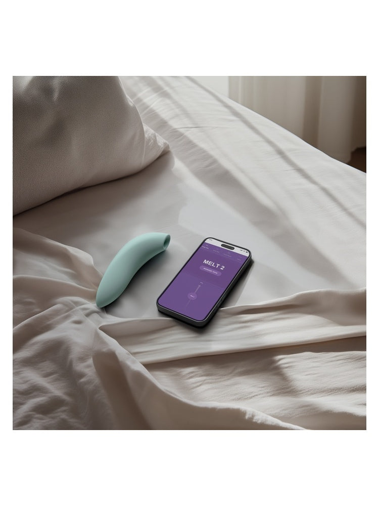 We-Vibe Melt 2 i mintgrønn på seng ved siden av smarttelefon med app.