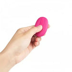 Hand holding a pink remote-control shaped intimate massager against a white background.
