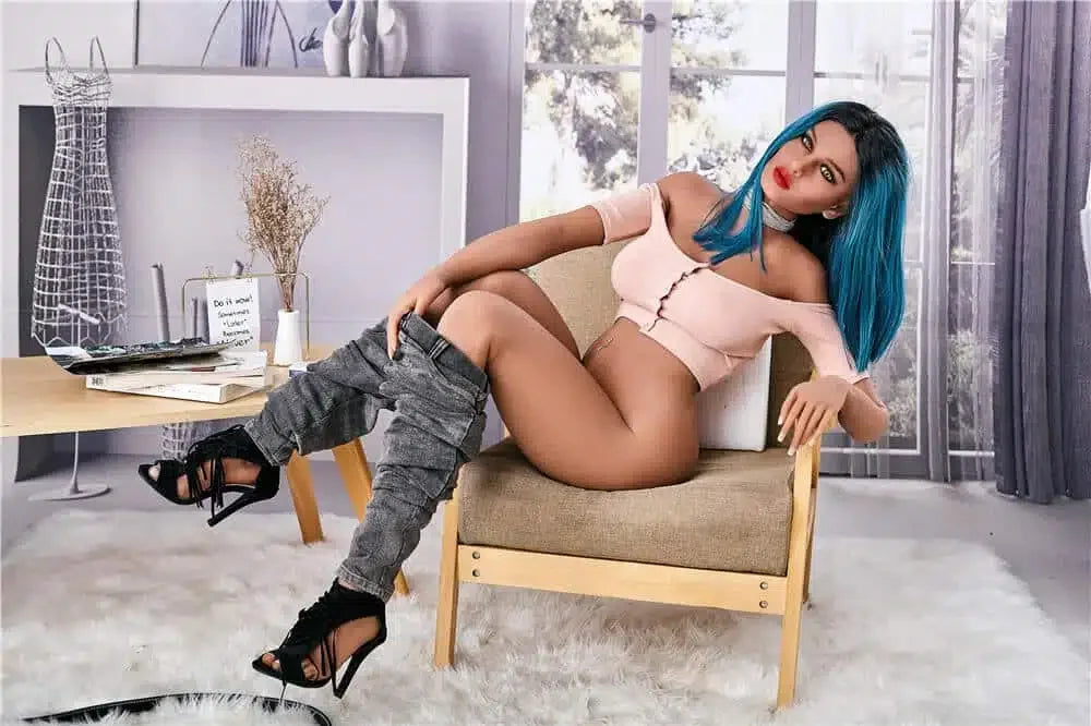 Realistic female doll with blue hair, pink top, and heels sitting on a chair in a modern room