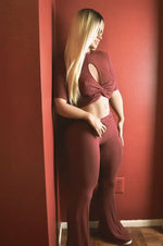Woman in ribbed burgundy lounge set with cutout top, standing against red wall.