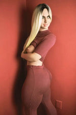 Realistic female mannequin with long blonde hair in ribbed burgundy lounge set against red wall